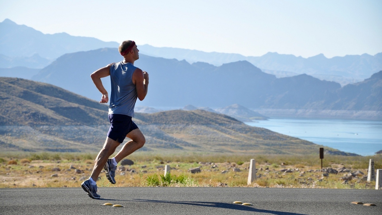 A man running on the road, with mountain ranges and water in the distance