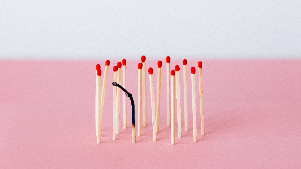 A group of new matches standing upright, with one burnt match, on a pink table.