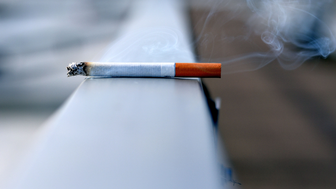 A lit cigarette lying on a dark grey handrail