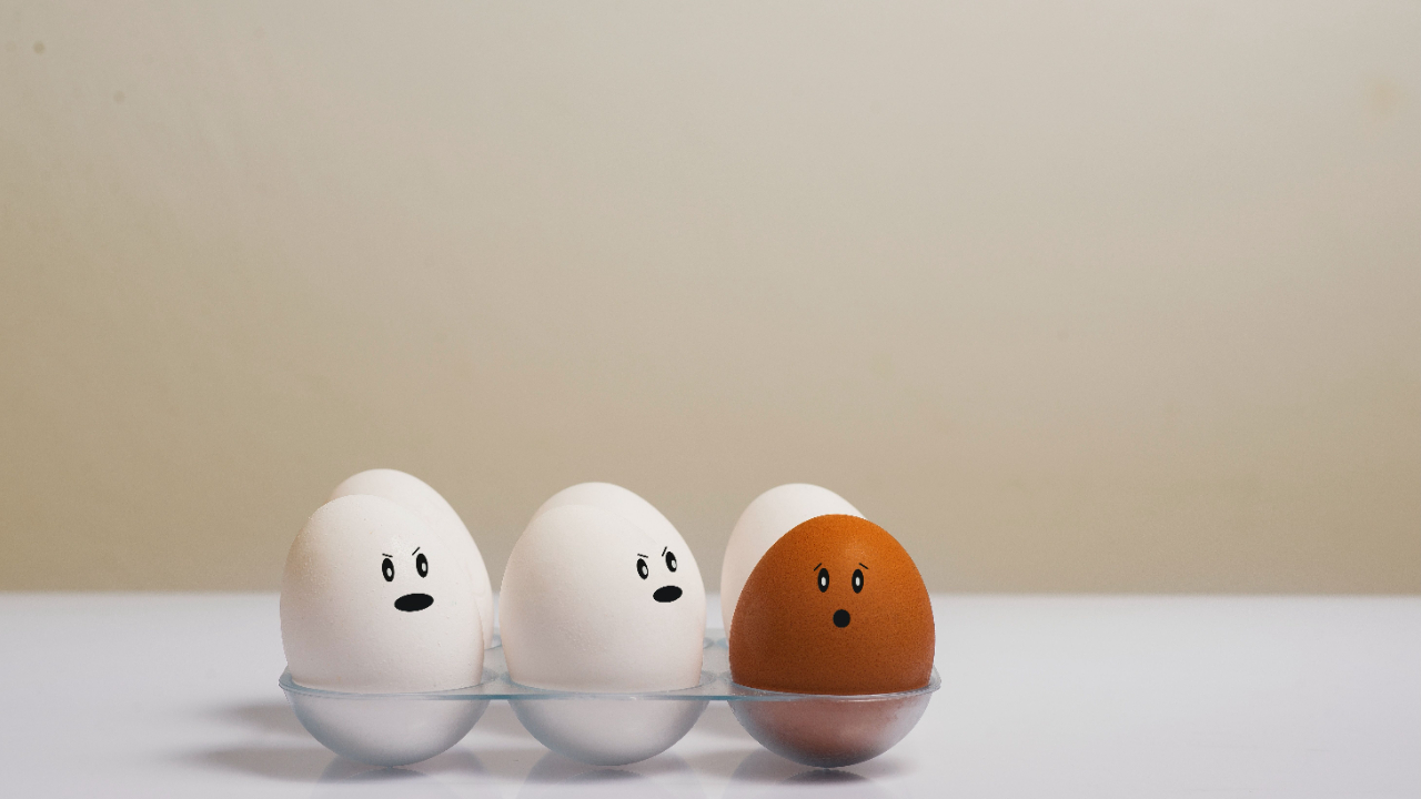 Two white eggs and one brown egg with animated faces in a glass dish on a white bench