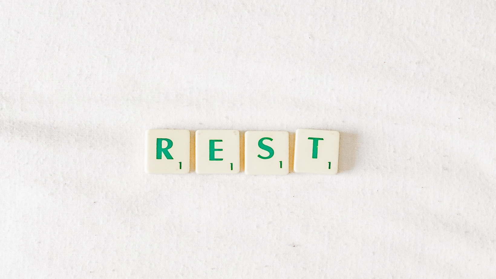 Cream and green scrabble tiles laying on a white background spelling 'rest'