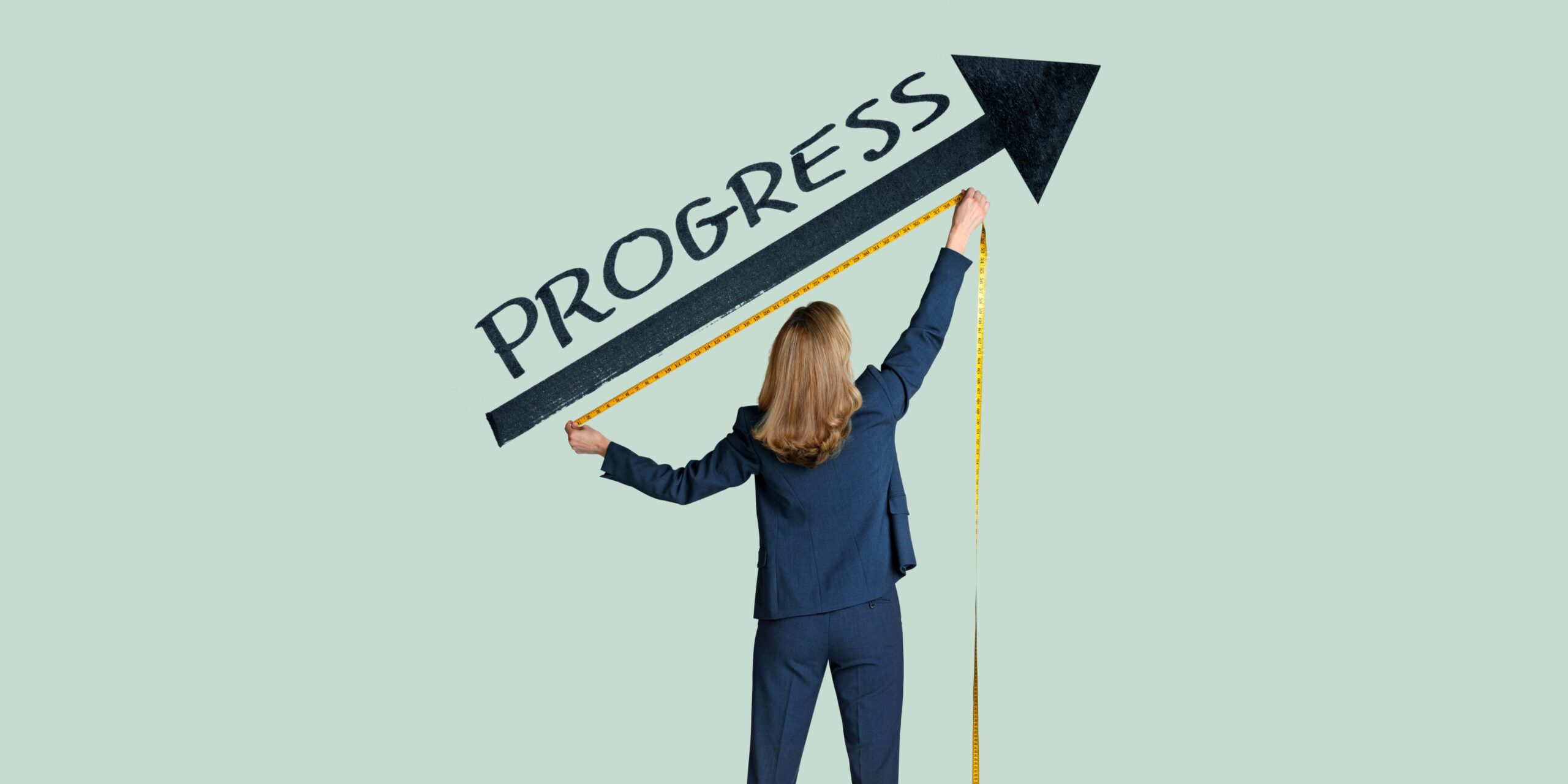 A lady dressed in a business suit holding a yellow tape measure. The word 'progress' is on the wall on top of a black arrow