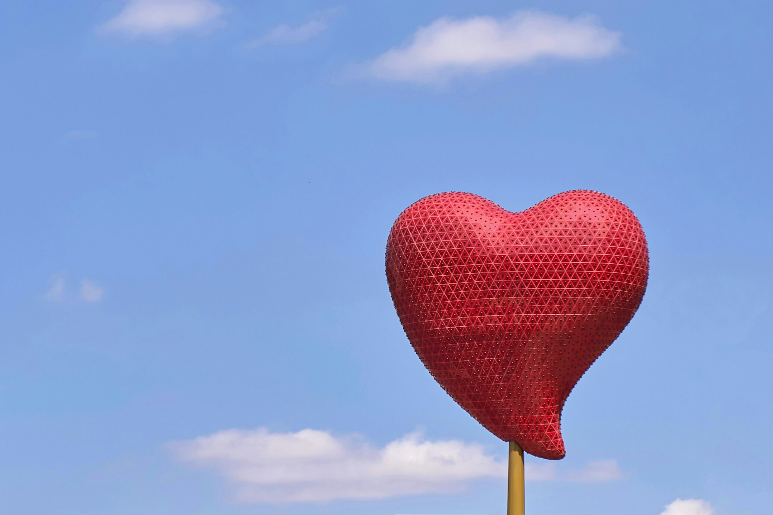 A red heart on a post in front of blue sky