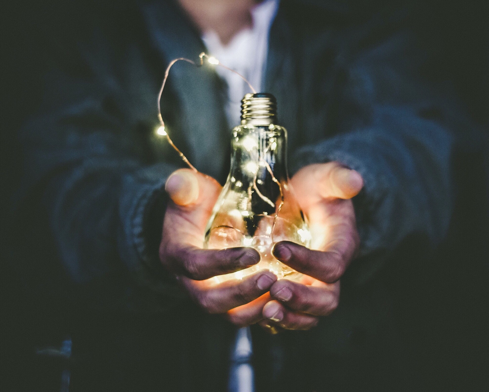 Male hands holding a lightbulb with lit fairy lights inside it