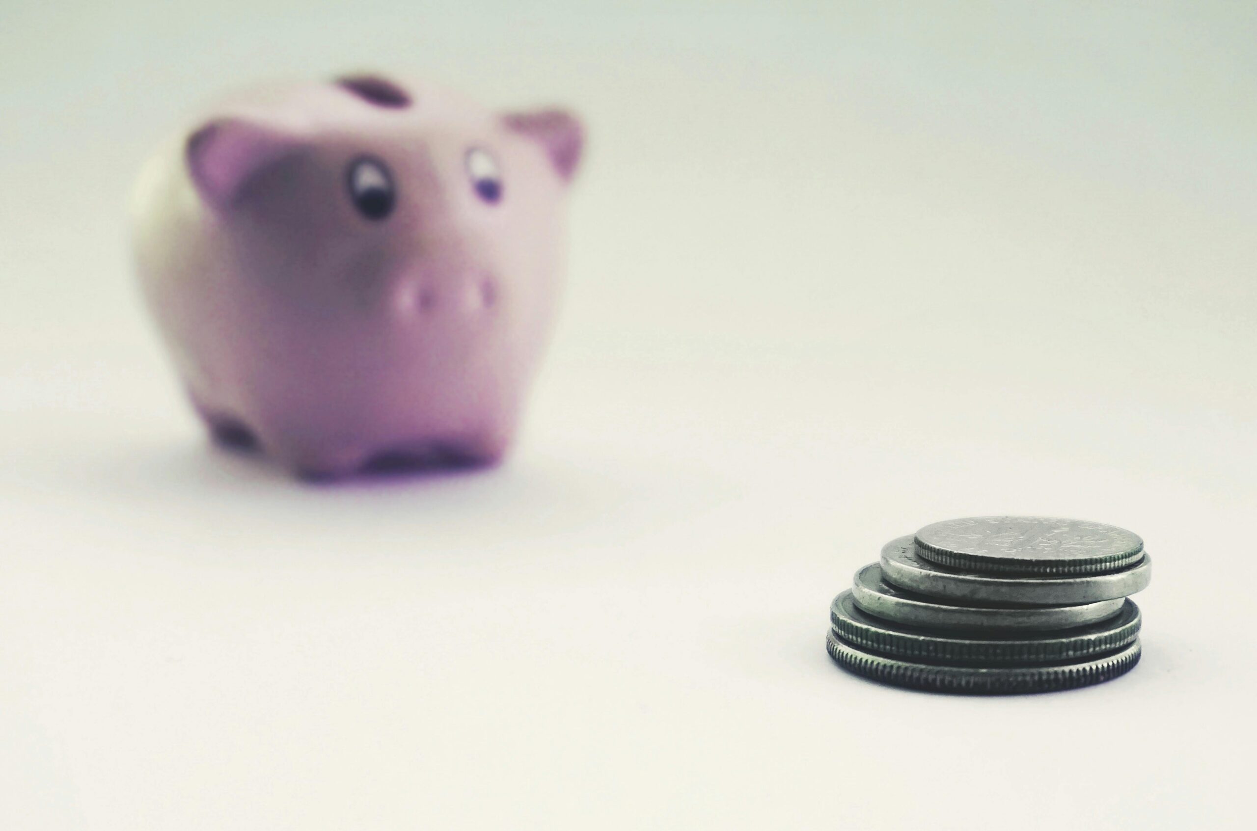 A purple piggy bank positioned to the far left of a stack of 5 silver coins