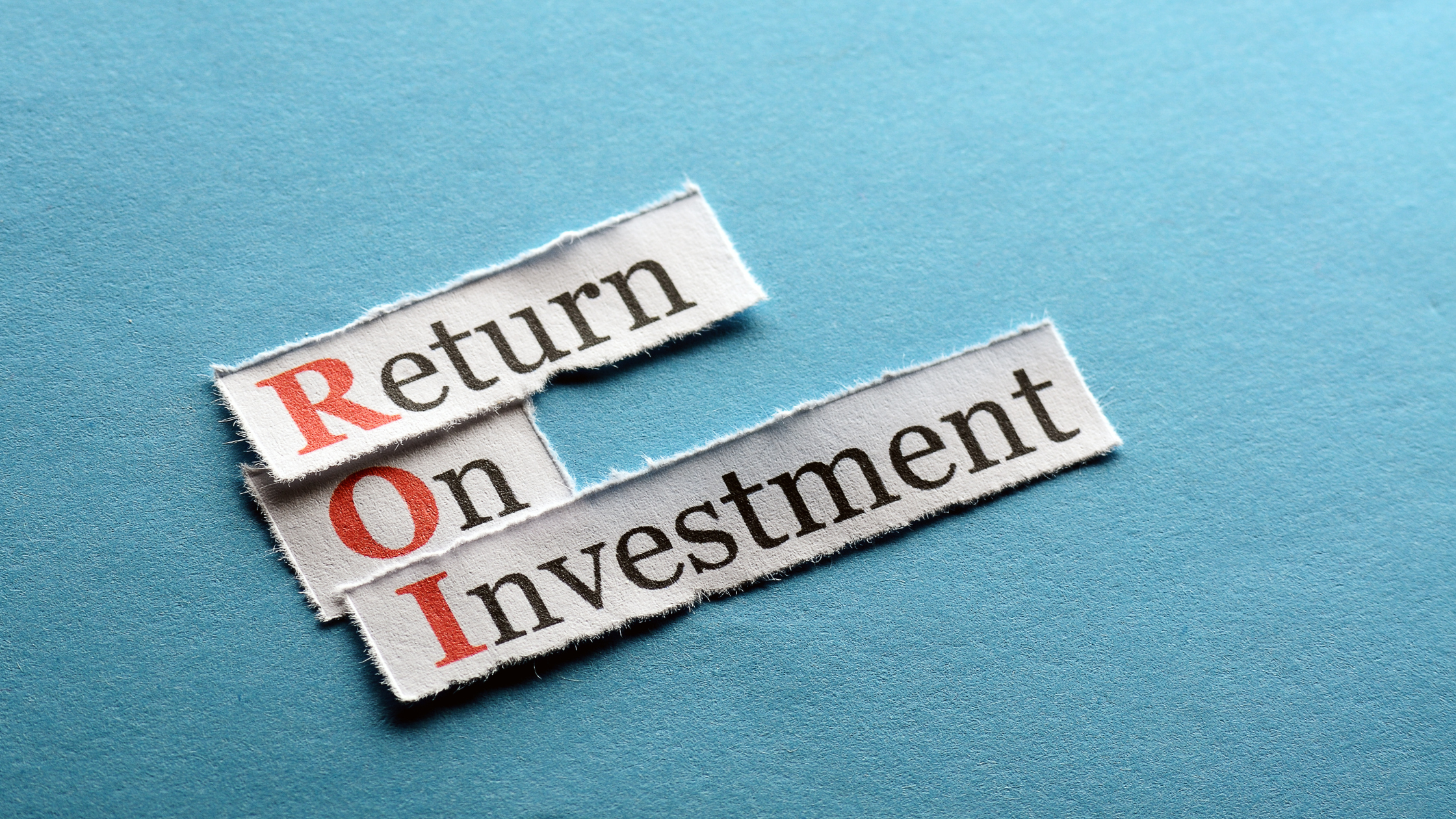 A blue background with the words 'return on investment' in black ink on pieces of white fabric. The letter 'R', 'O' and 'I' are in red ink.