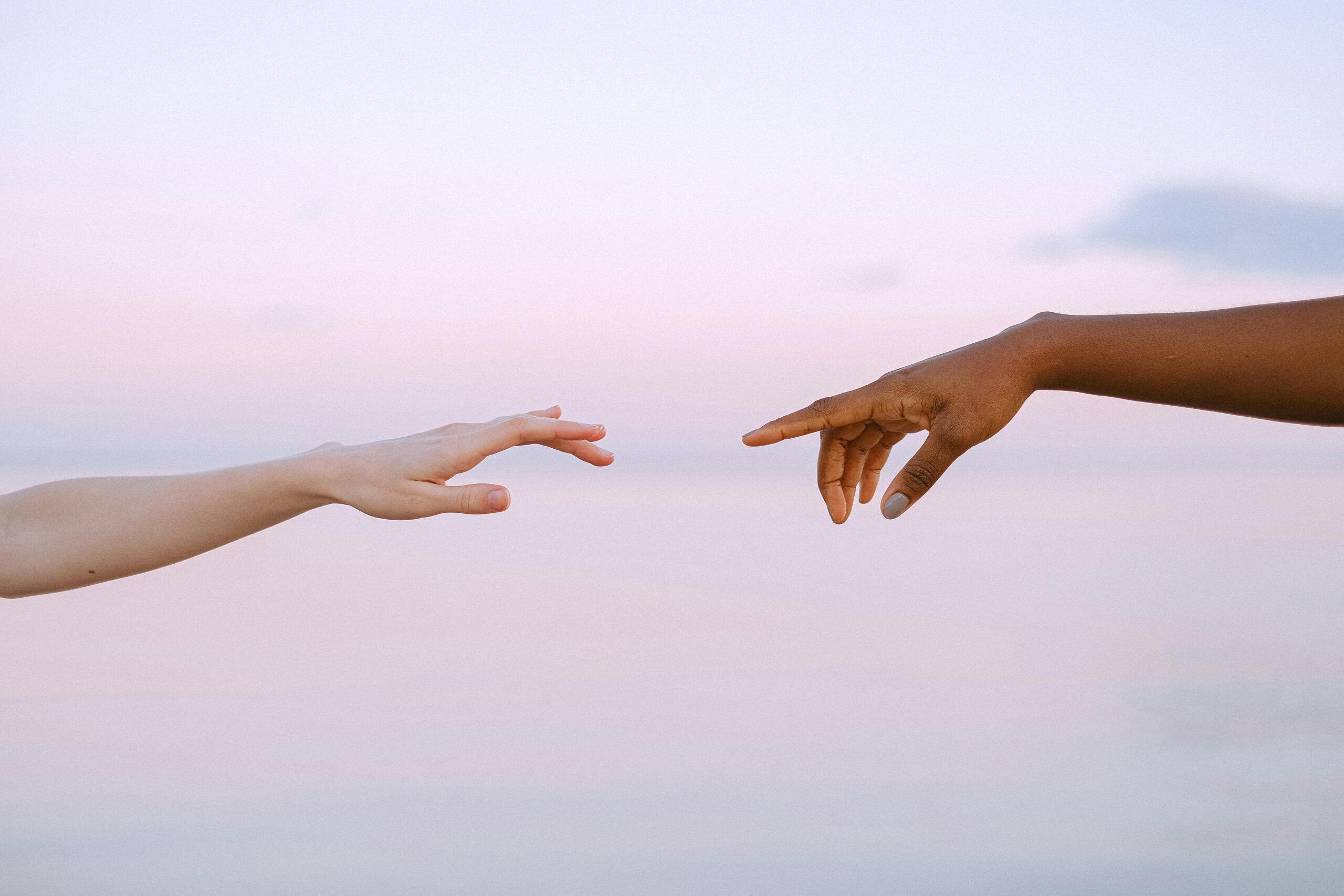 two hands outstretched towards each other with a pink sky in the background