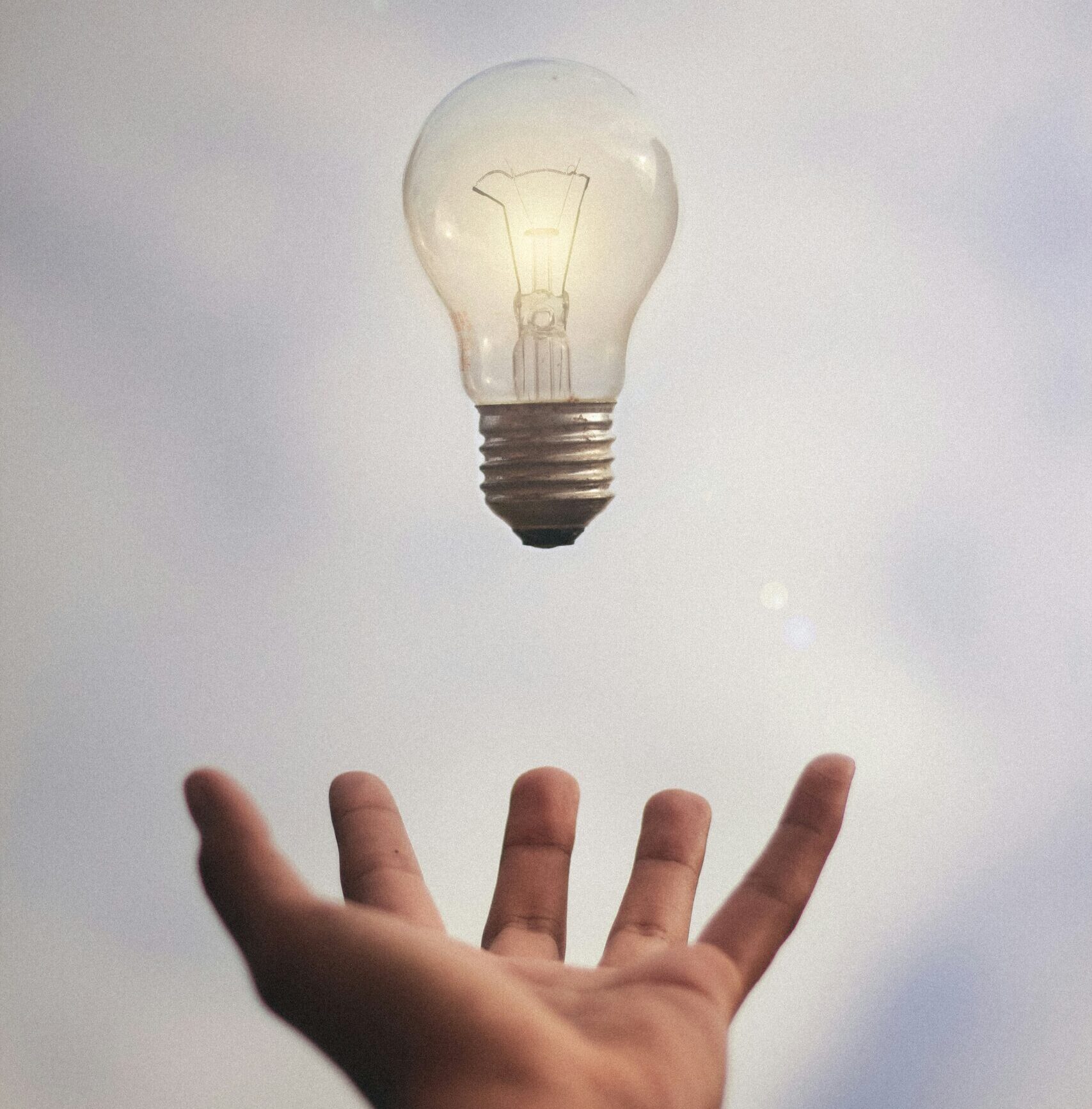 Hand reaching towards a floating light bulb, symbolising creative ideas and innovation
