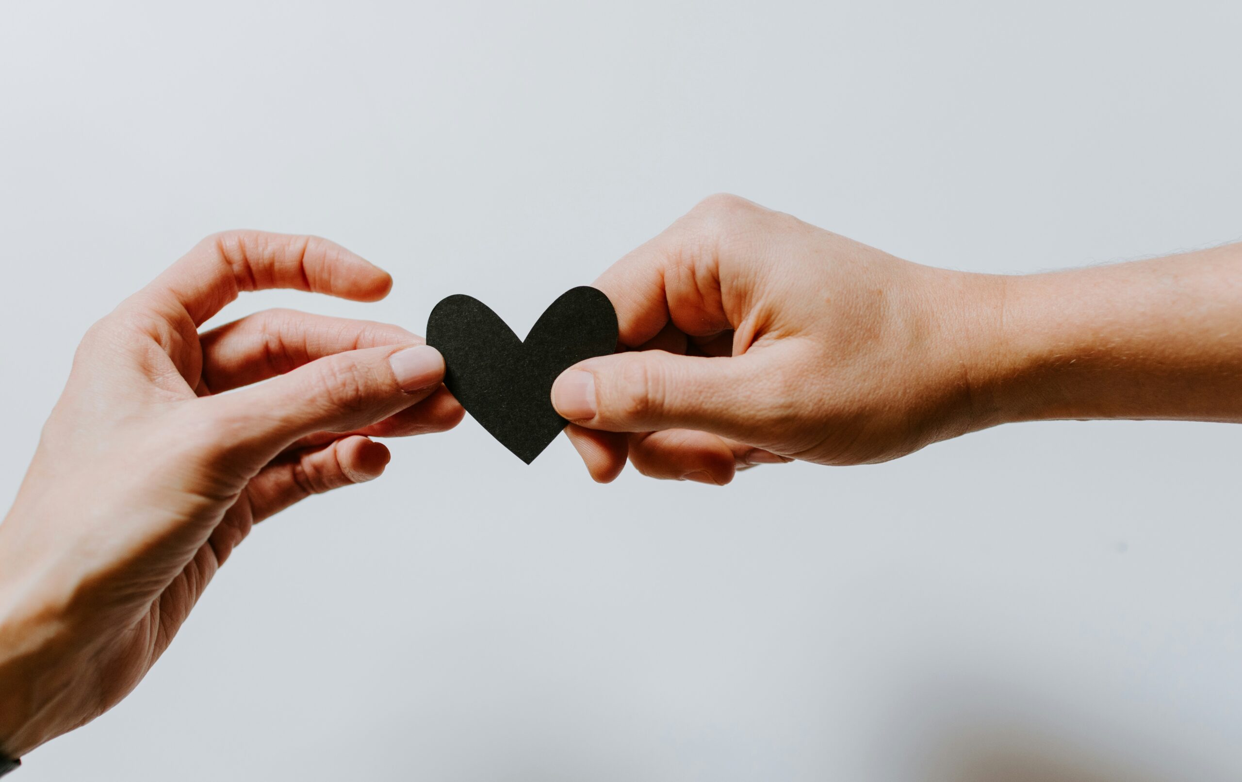 Two hands holding a small black heart against a neutral background