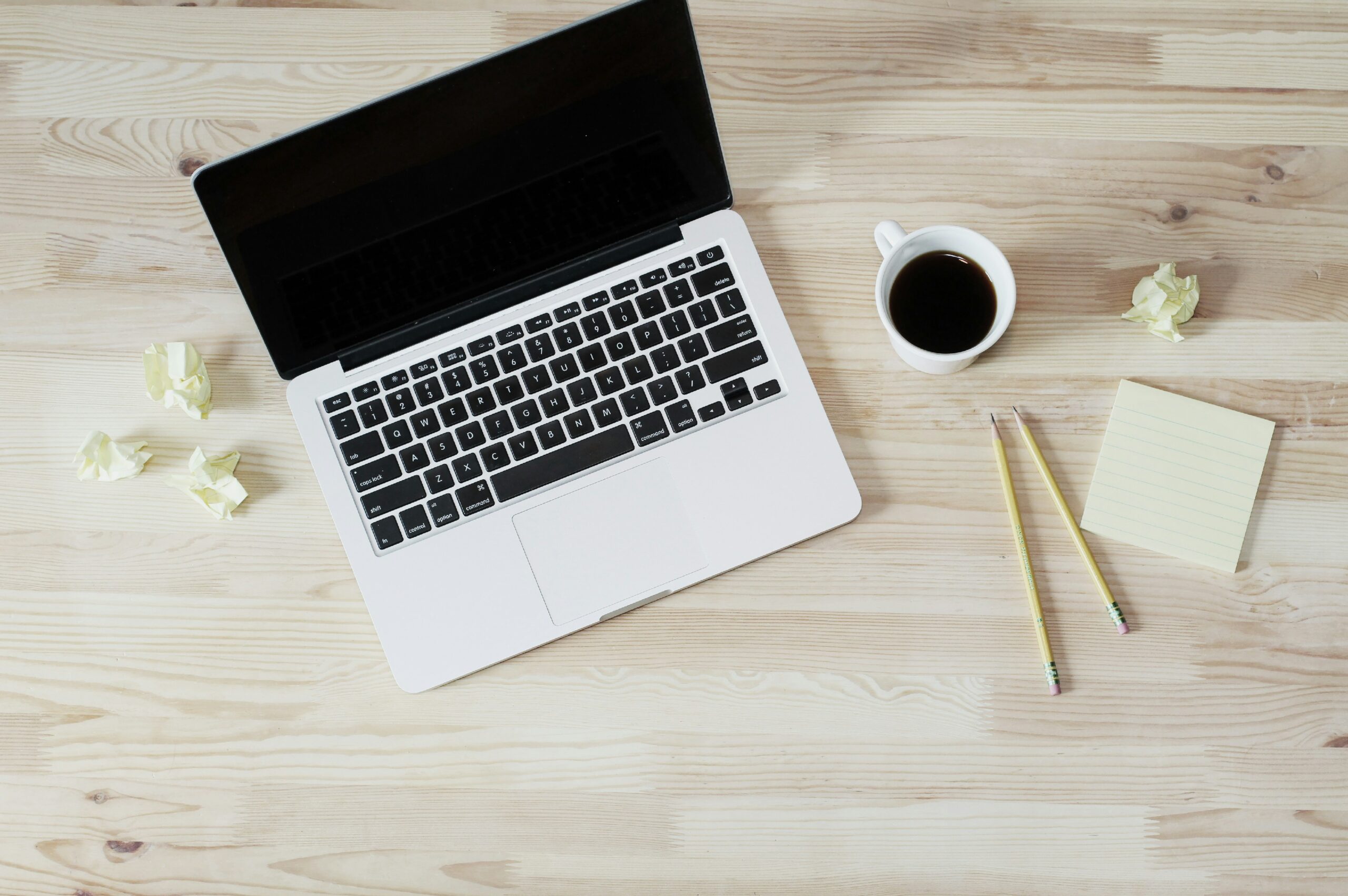 Laptop on a wooden desk with coffee, pencils and notepad